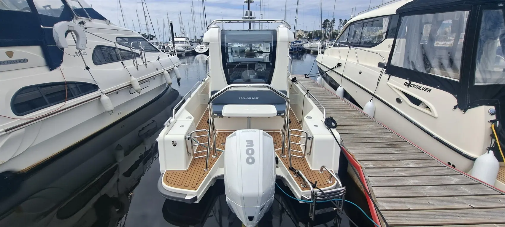 A modern boat with a Mercury 300 engine is docked at a marina, surrounded by other boats and water.